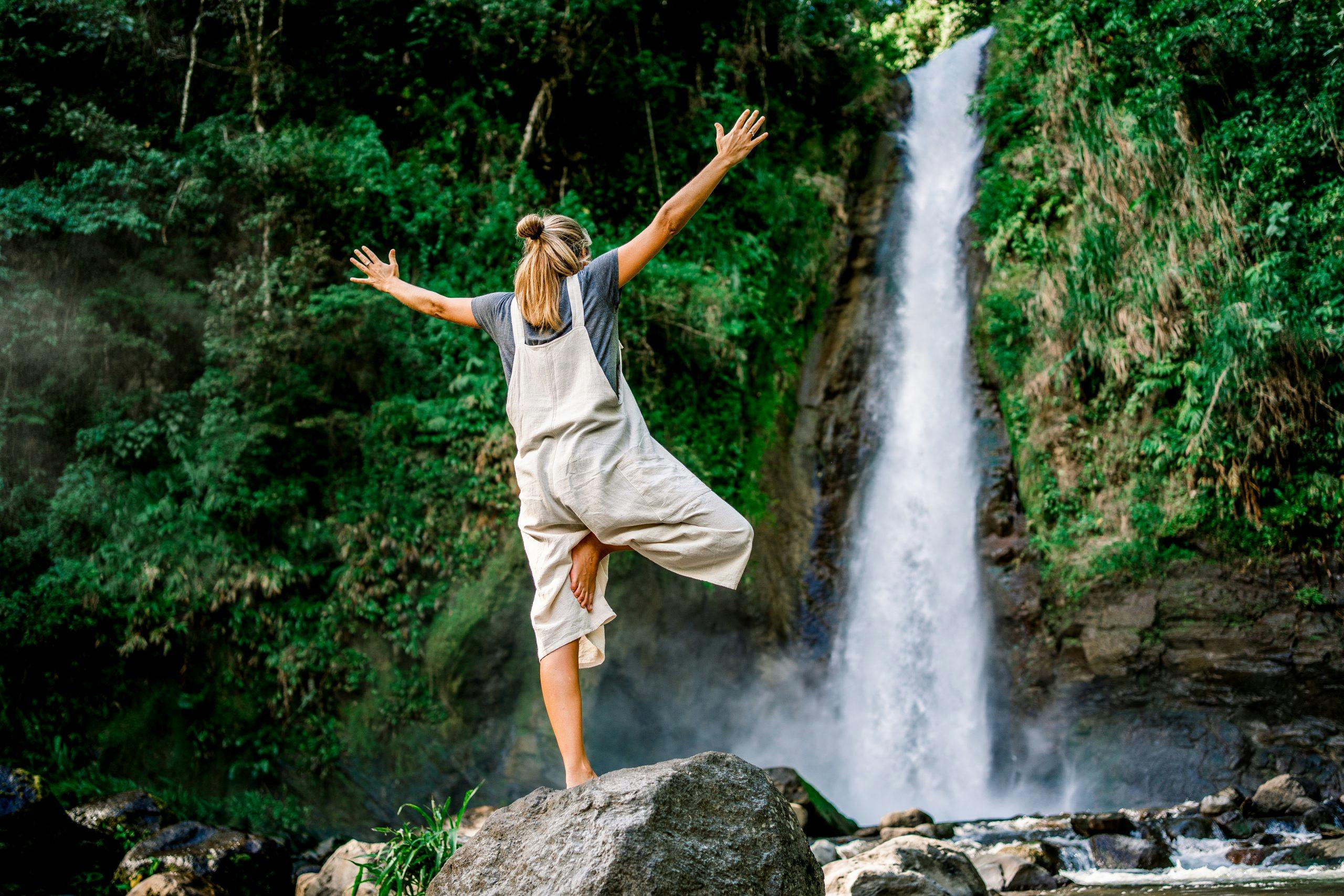 Young caucasian woman standing in a yoga pose in front of a waterfall in the middle of the jungle