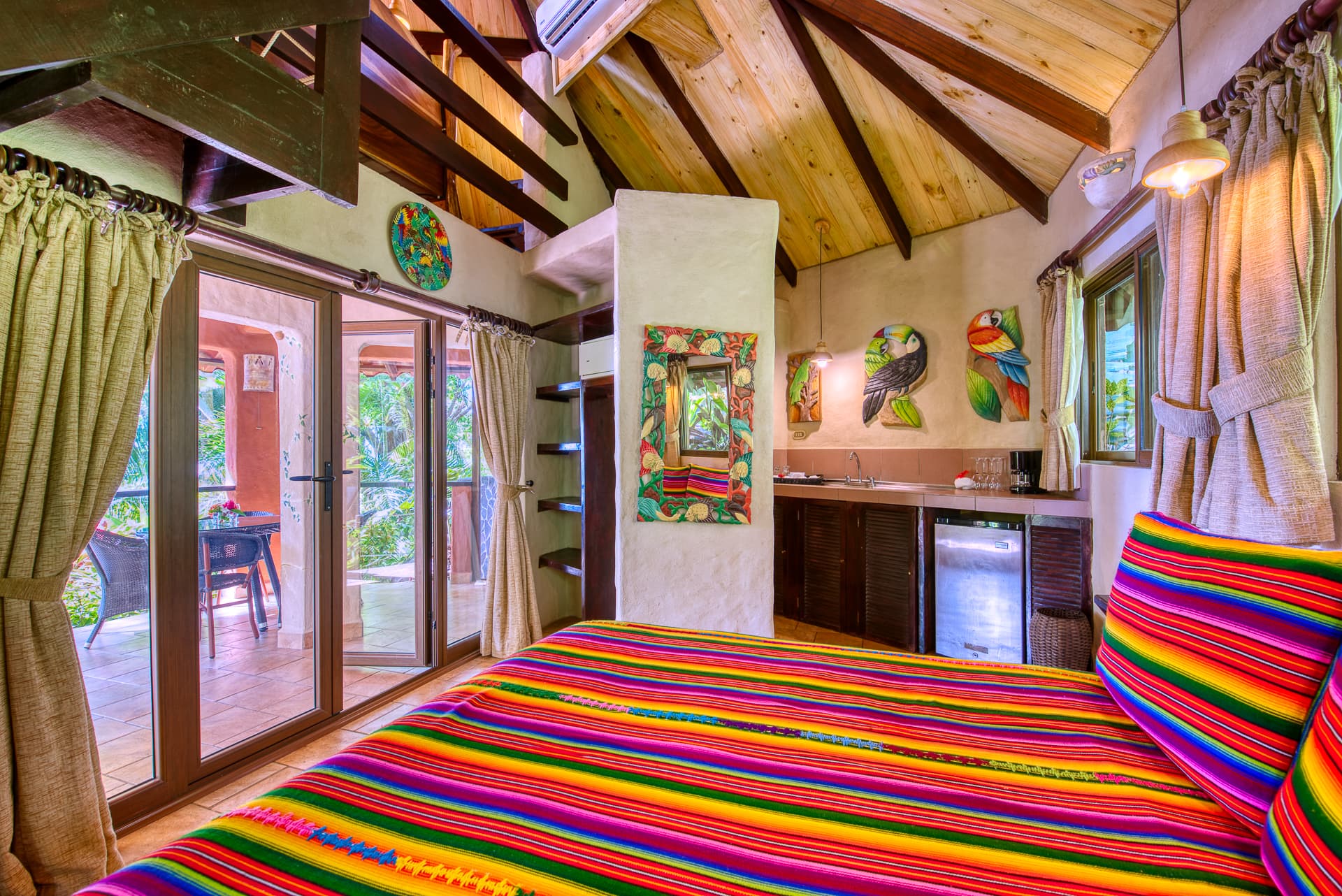 Coco Joe's Bungalow Interior with bed made with brightly striped bedding, vaulted ceilings and sliding doors leading to sitting area on private patio