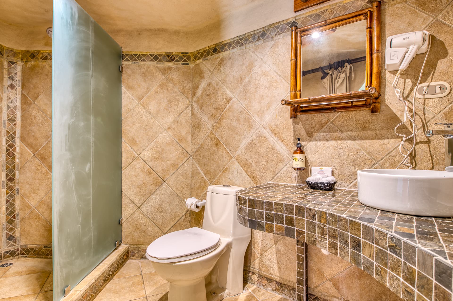 Gorgeous tiled bathroom in earth tones with shower, toilet, and curved tiled vanity with vessel sink