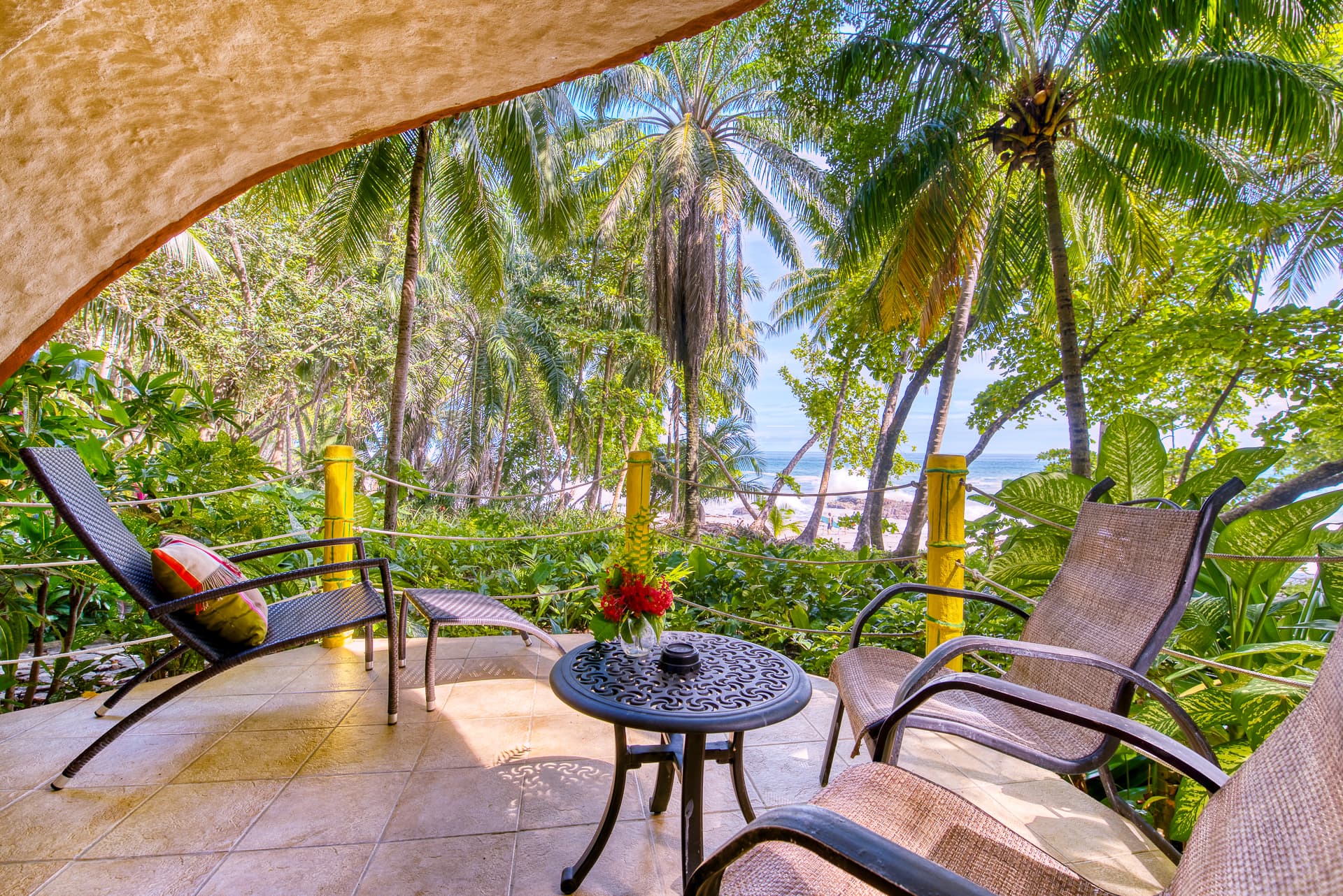 Open-air patio with table and chairs surrounded by palm trees with ocean views