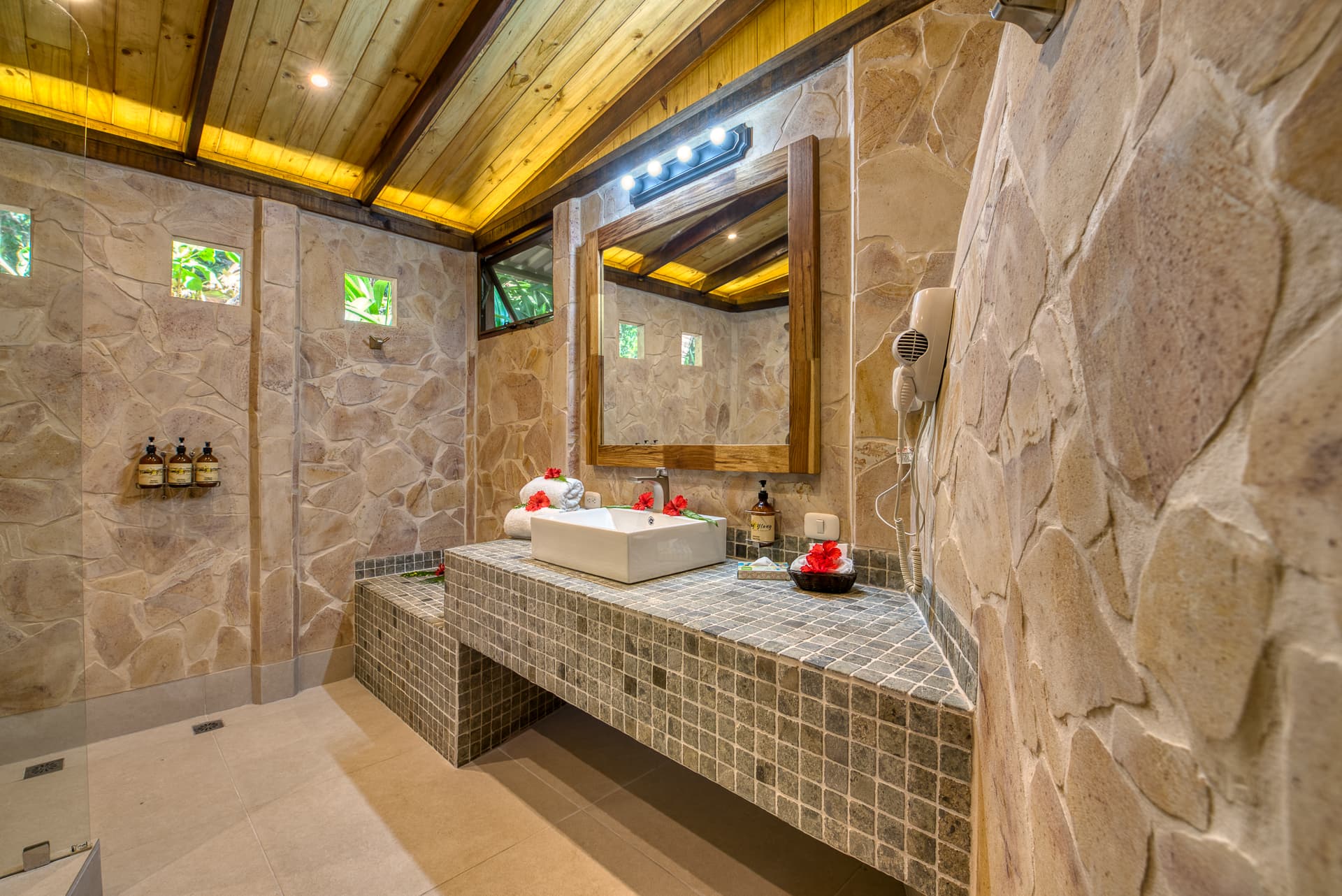 Stunning bathroom with rock walls with tiled vanity and white sink with lighted mirror