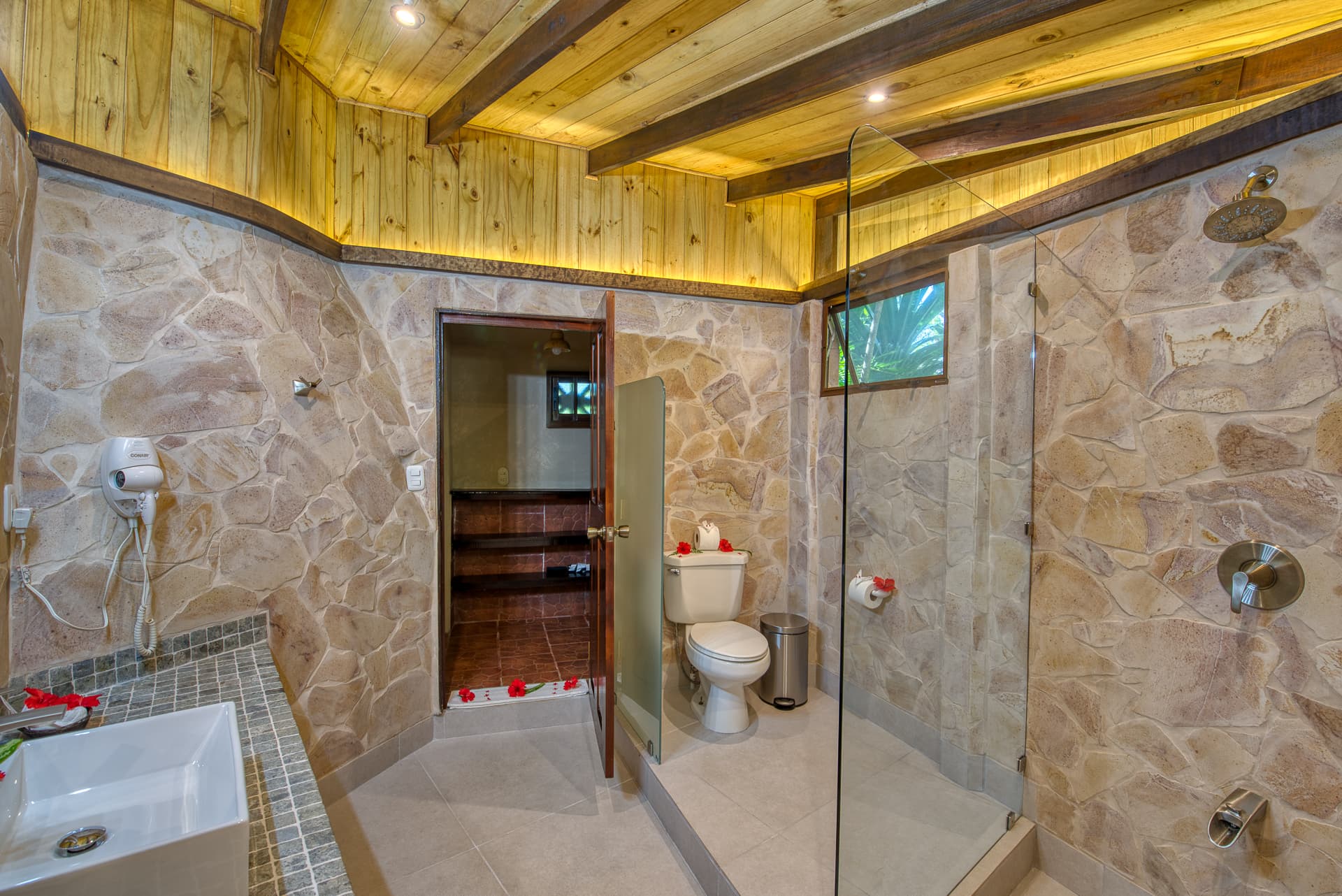 Bathroom with rock walls, glass-enclosed shower, toilet, and tiled vanity with sink