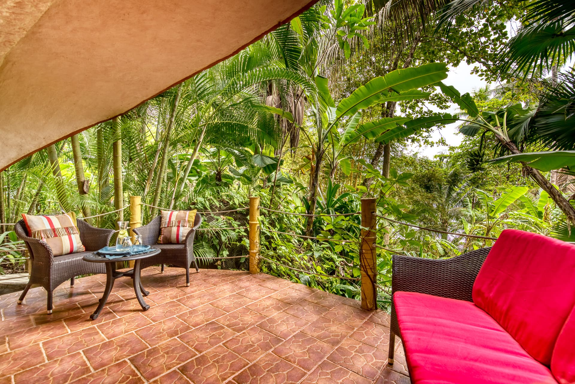 Open-air private patio with outdoor chairs and loveseat with jungle views