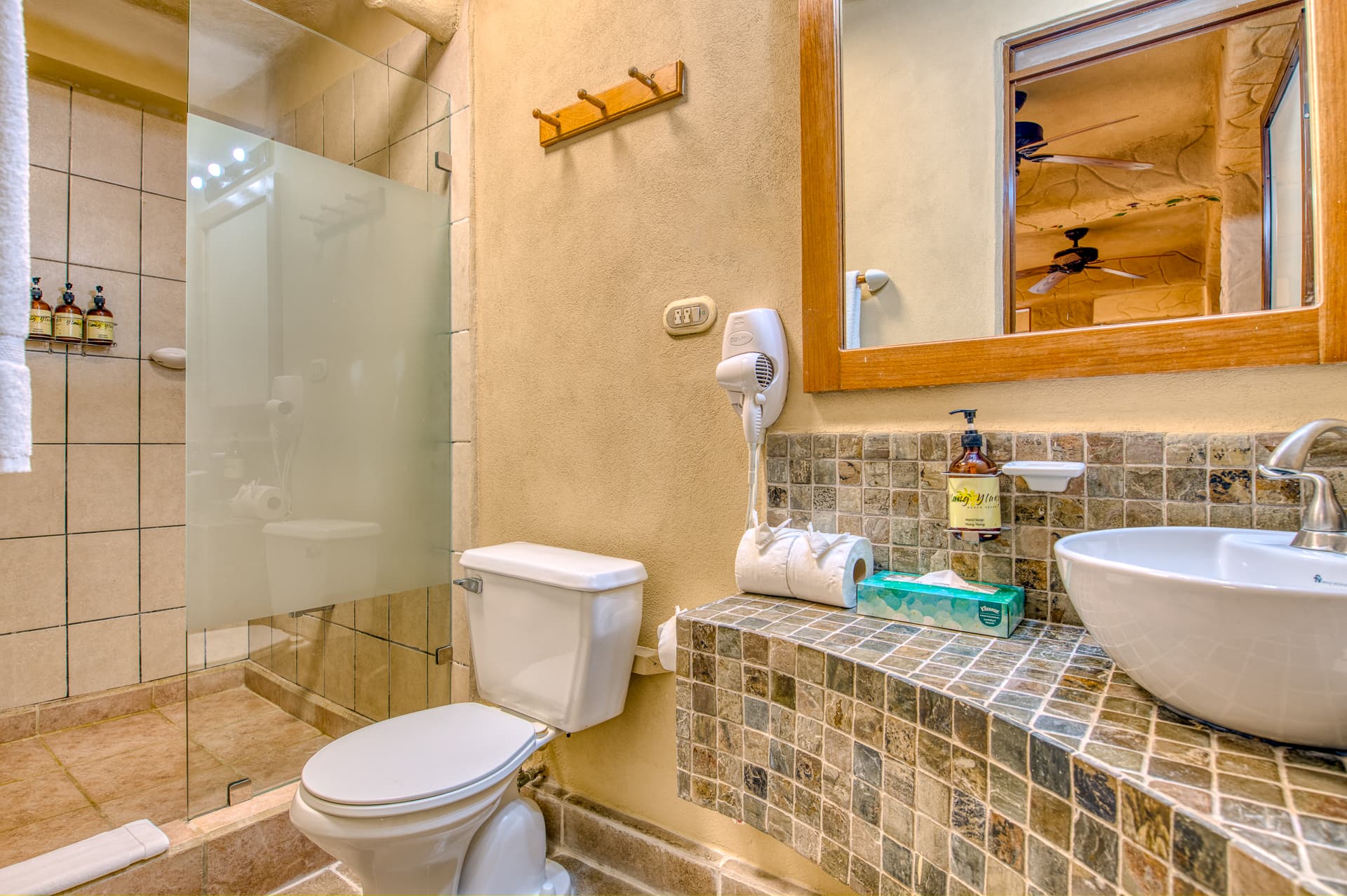 Spacious bathroom with tiled, glass-enclosed shower, toilet, tiled vanity and vessel sink