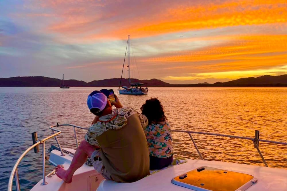 A couple gazing over the rail of a boat deck at the sunset over the ocean waters