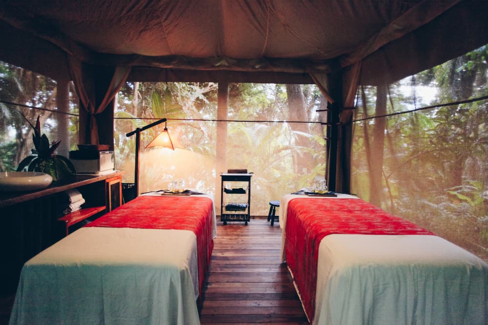 Two massage tables side-by-side in a screened-in cabana surrounded by tropical foliage