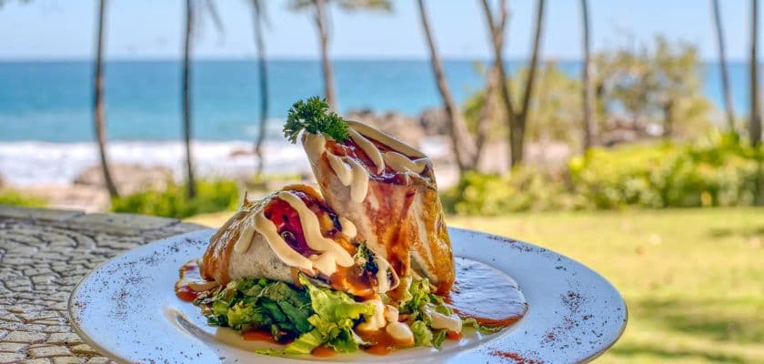 A delicious burrito with toppings, served on a plate with a scenic beach background.