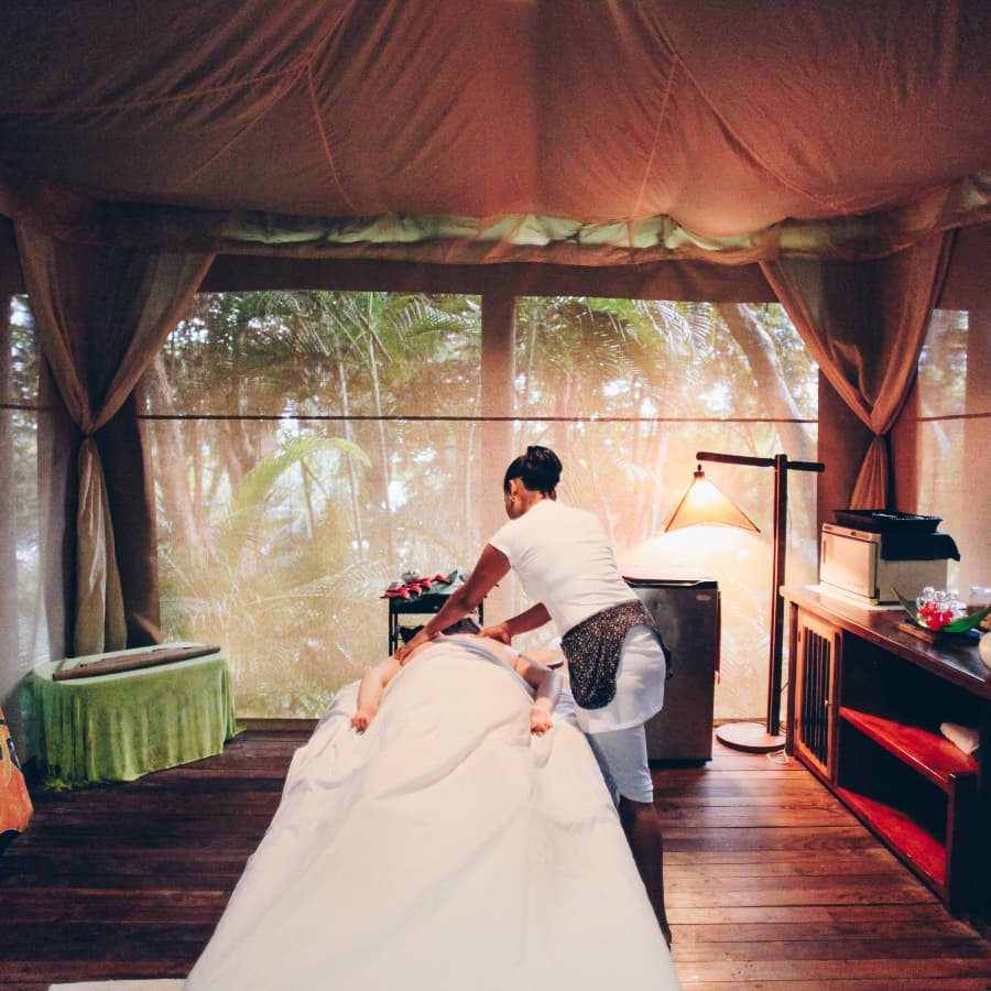 A female masseuse massaging a person's back on a massage table in a jungle cabana