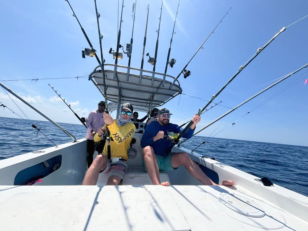 Four fishermen on a boat hold fishing rods under a clear blue sky.