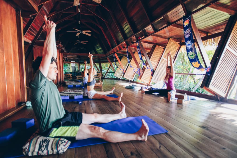 Several people sitting with their legs stretched out in a V with their hands clasped over their heads