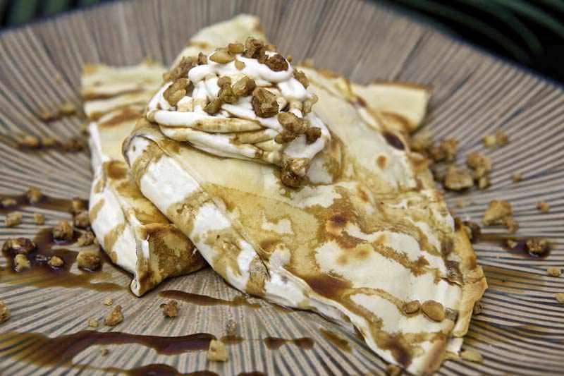 A plate of crepes topped with whipped cream, caramel drizzle, and chopped nuts.
