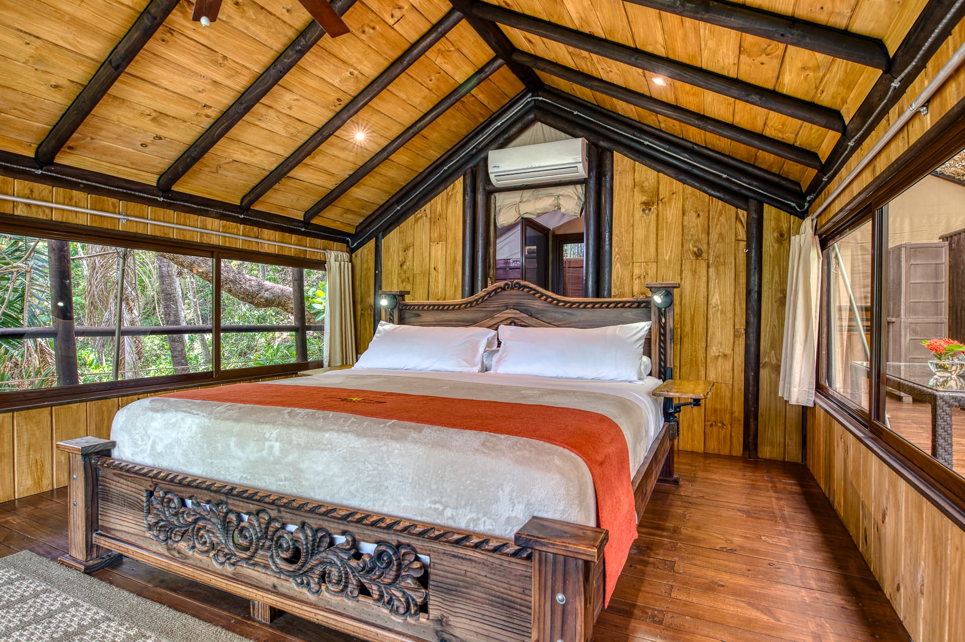 Cozy wooden bedroom featuring a carved bed and large windows.