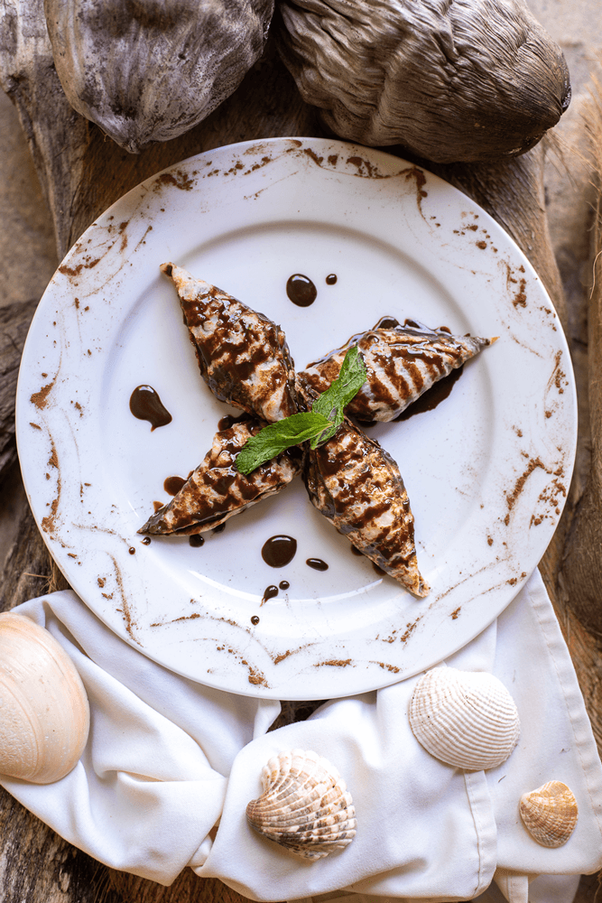 Star shaped pastry with chocolate sauce on white plate on wood table with sea shells as decoration.