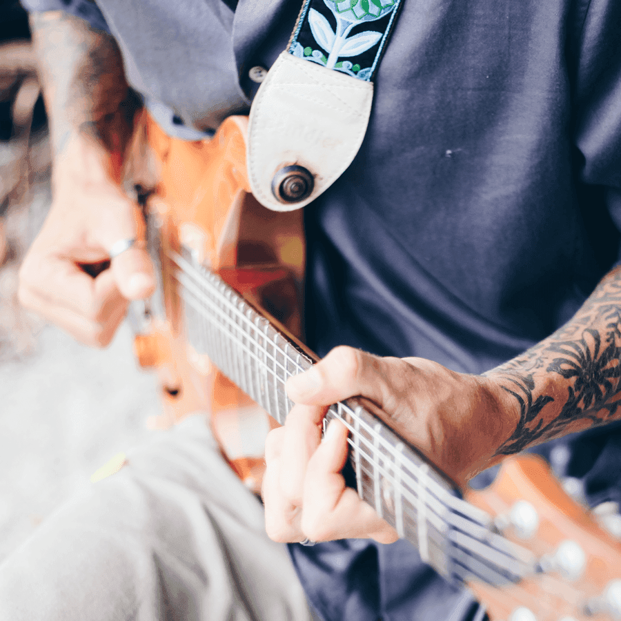A close-up of a person playing an orange electric guitar, focusing on their hands.