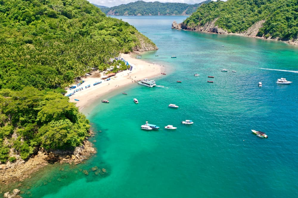 Brilliant blue ocean waters filled with a variety of boats near an island beach