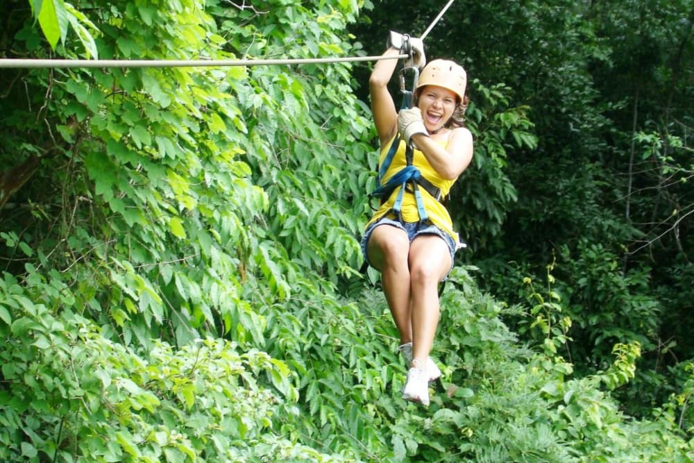 A woman with a big grin on a zipline above tropical trees