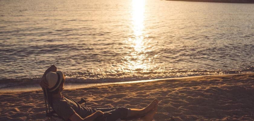 Person relaxing on a beach chair as the sun sets over the water.