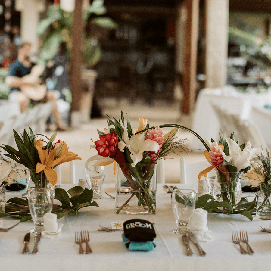 Tropical Flowers arranged on table with place settings on top of white table cloth