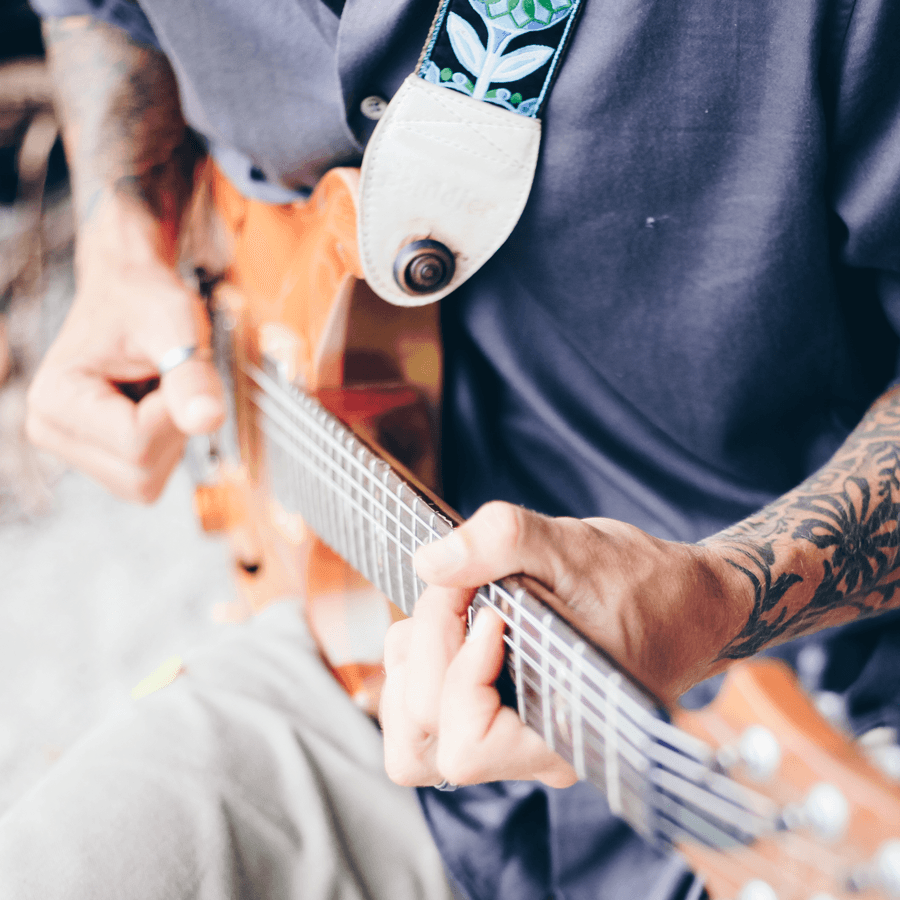 Man with tattoos, sitting playing guitar in blue shirt