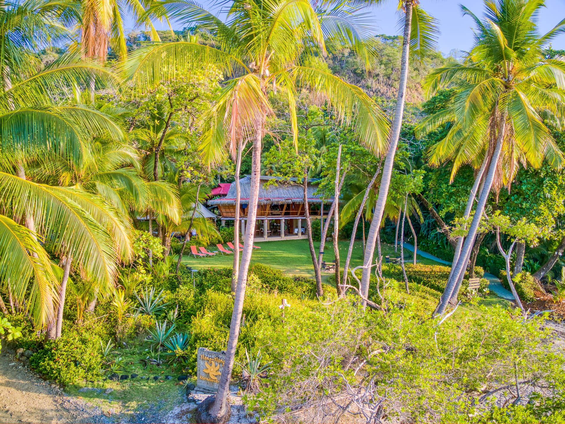 A secluded paradise featuring a beachfront villa surrounded by lush greenery and swaying palm trees.