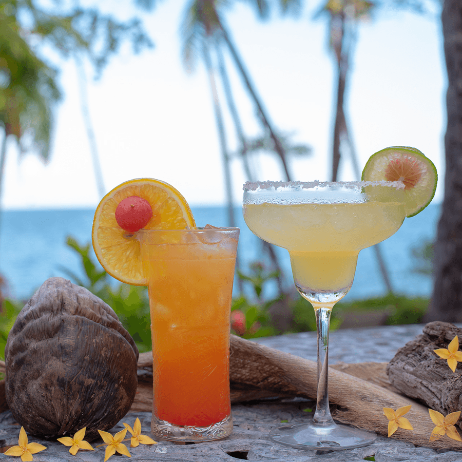 Tropical adult beverages garnished with fresh fruits and the bar with the ocean in the background
