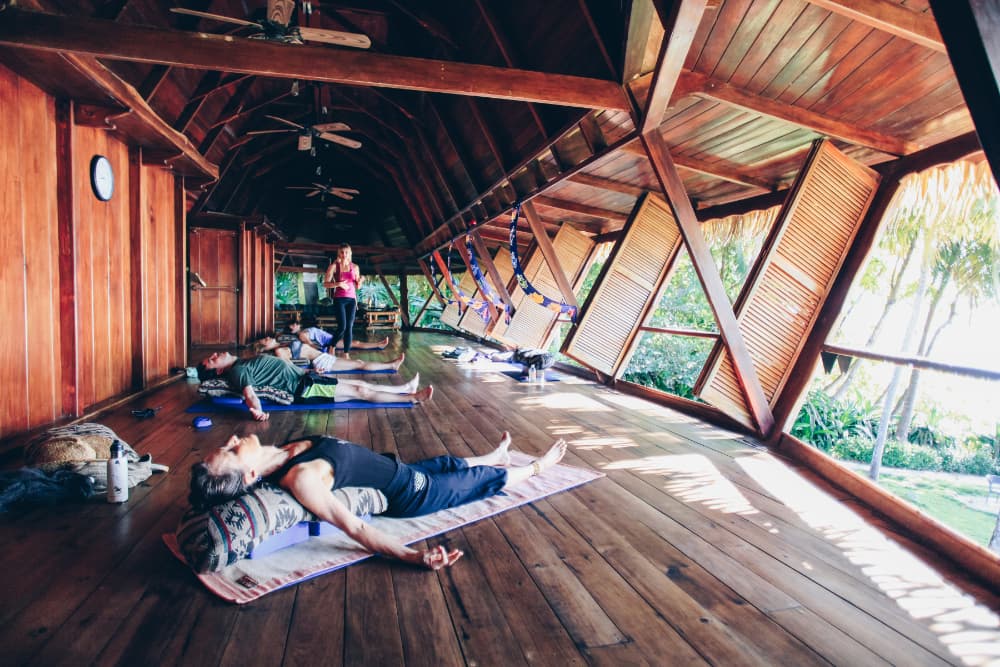 A small group of people lying on their backs on yoga mats while an instructor stands nearby
