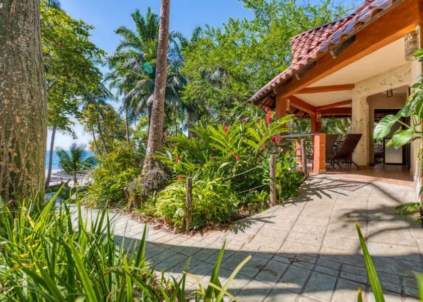 A picturesque garden pathway leads to a charming house near the beach, surrounded by lush tropical plants. A picturesque garden pathway leads to a charming house near the beach, surrounded by lush tropical plants.