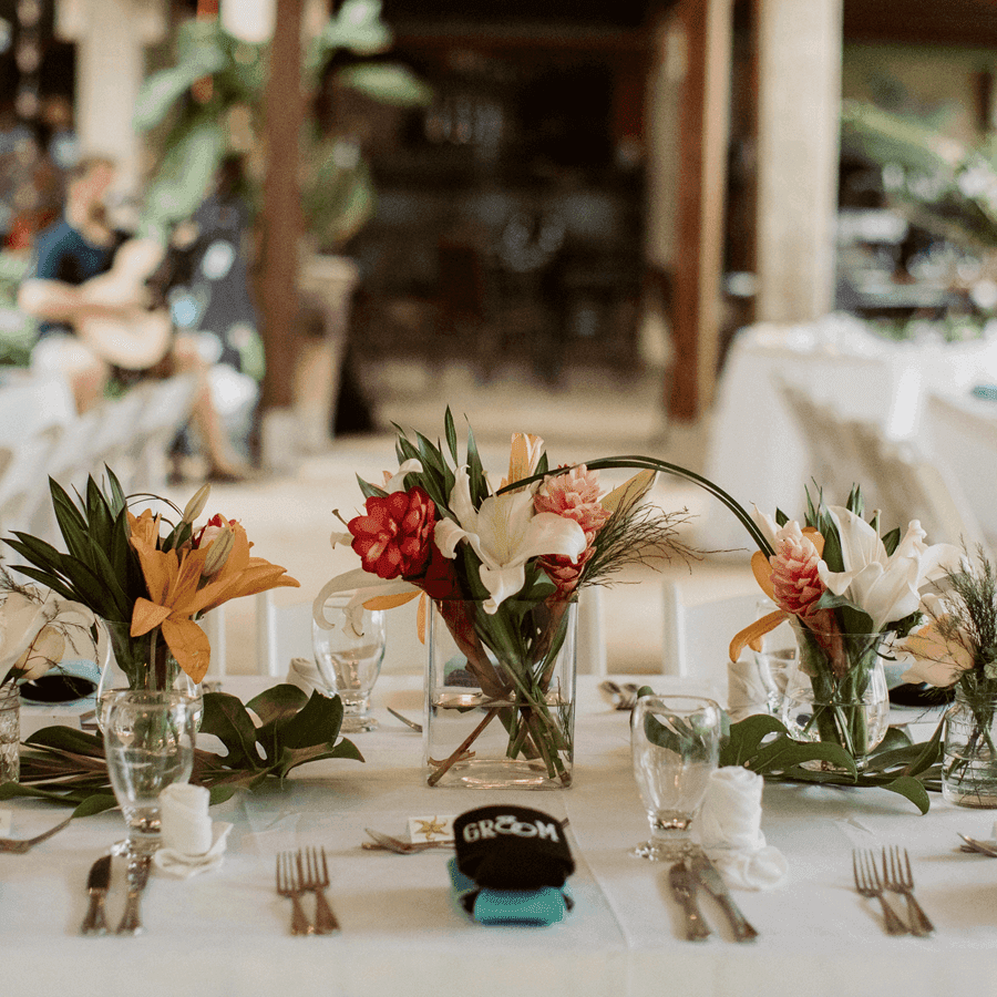 A beautifully set dining table adorned with vibrant floral centerpieces and a "GROOM" cap.