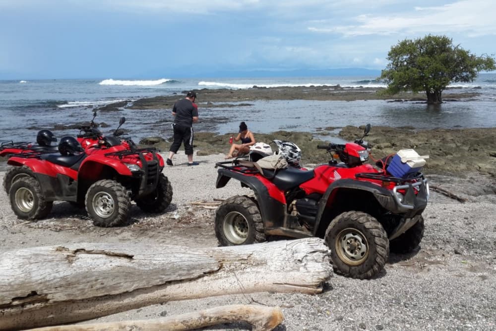Two people resting on a sandy beach with two red ATVs parked nearby
