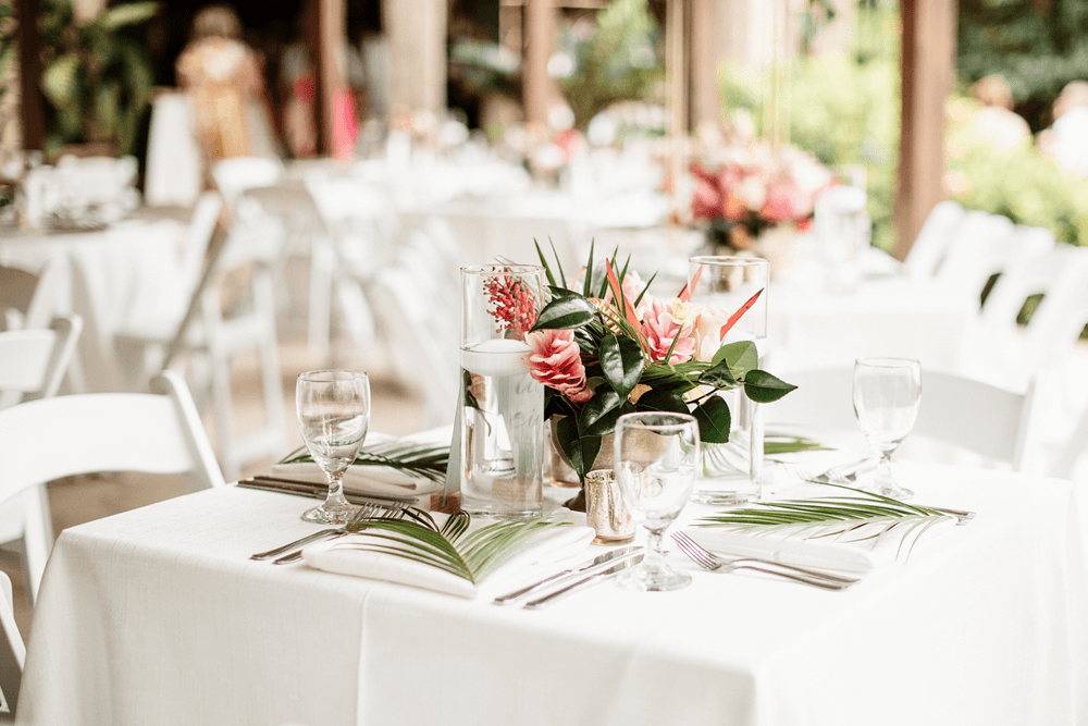 Tropical Flowers arranged on table with place settings on top of white table cloth