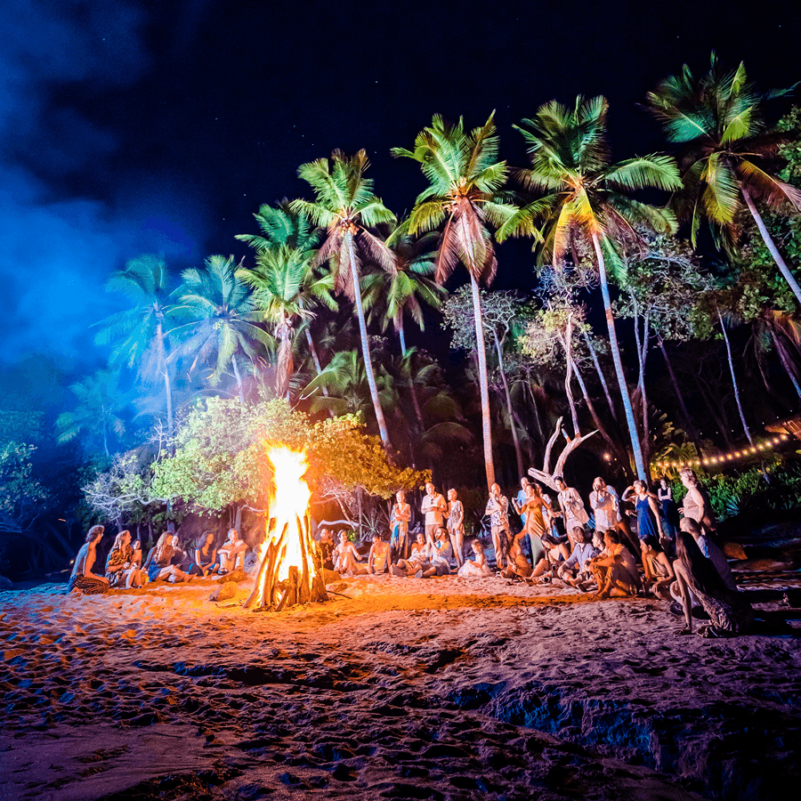 Man in dark spinning fire sticks with people sitting on grassy ground watching