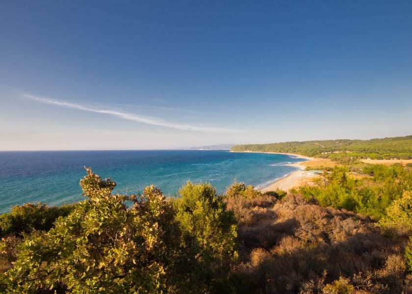 A panoramic view of a coastline with turquoise water and green vegetation under a clear blue sky. A panoramic view of a coastline with turquoise water and green vegetation under a clear blue sky.