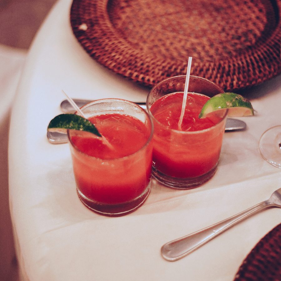 Two red alcoholic drinks on a table with straws