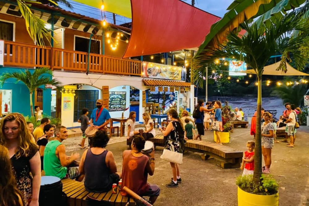 A festive town scene with brightly colored buildings and people mingling under palm trees