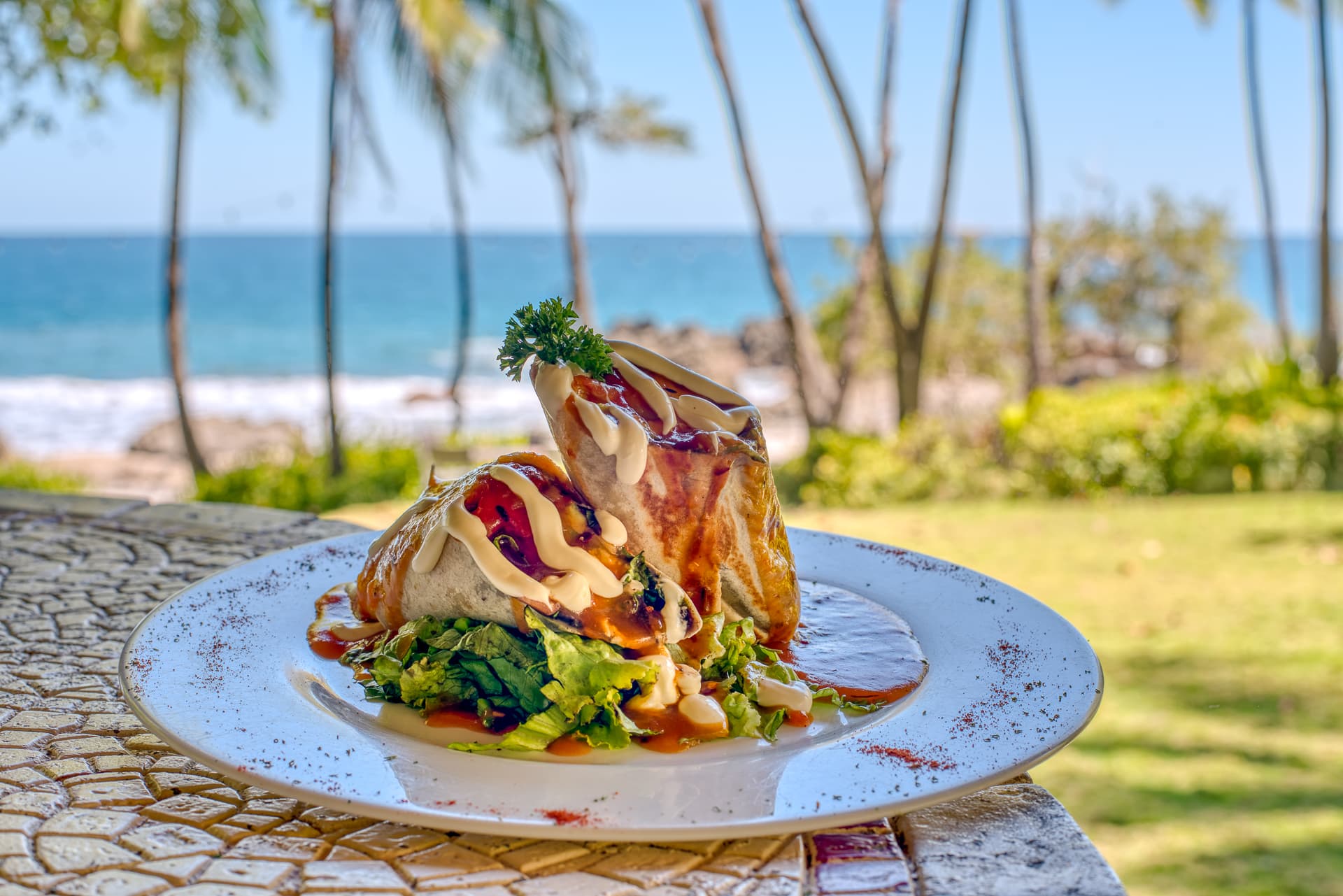 stacked seafood and vegetables on plate with ocean and palm trees in background