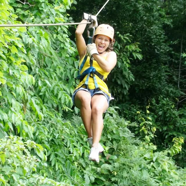A woman joyfully ziplining through lush green foliage.
