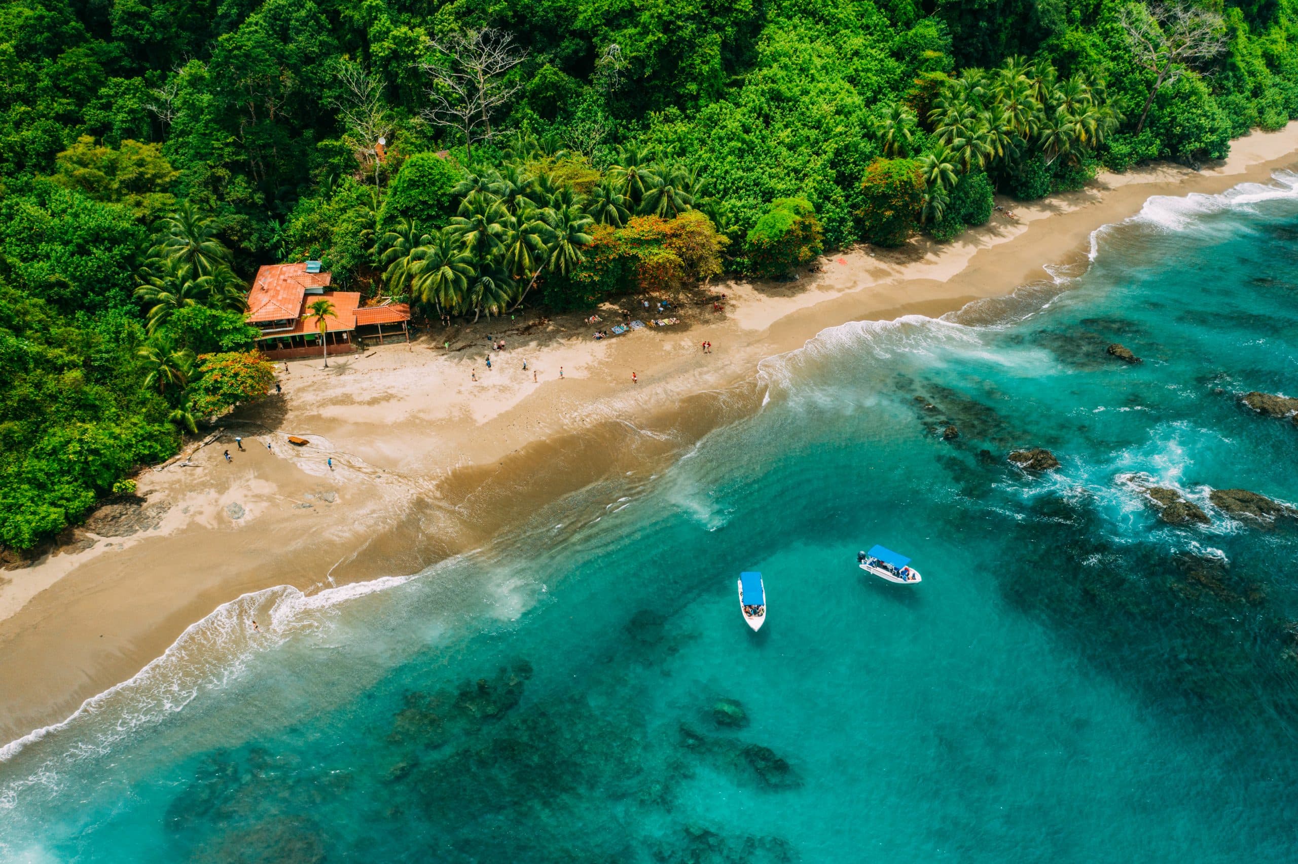Aerial view of a tropical beach with a small wooden cabin, surrounded by lush greenery and two boats on the water. Aerial view of a tropical beach with a small wooden cabin, surrounded by lush greenery and two boats on the water.