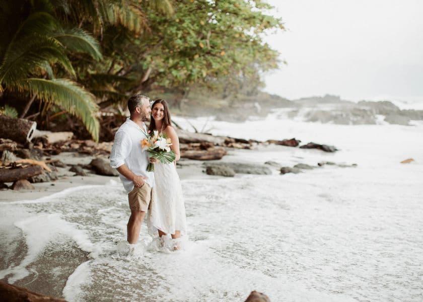 A couple enjoys the ocean waves while smiling at each other, with a lush coastline in the background. A couple enjoys the ocean waves while smiling at each other, with a lush coastline in the background.