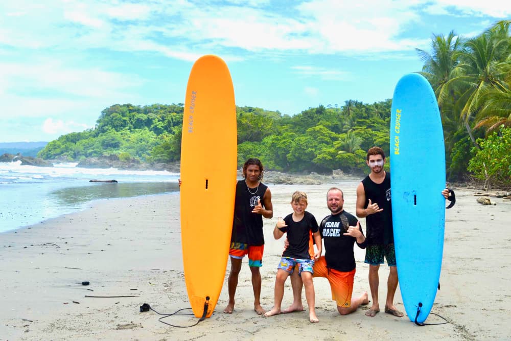 A group of four people of different ages in surf gear posing by surfboards on the beach