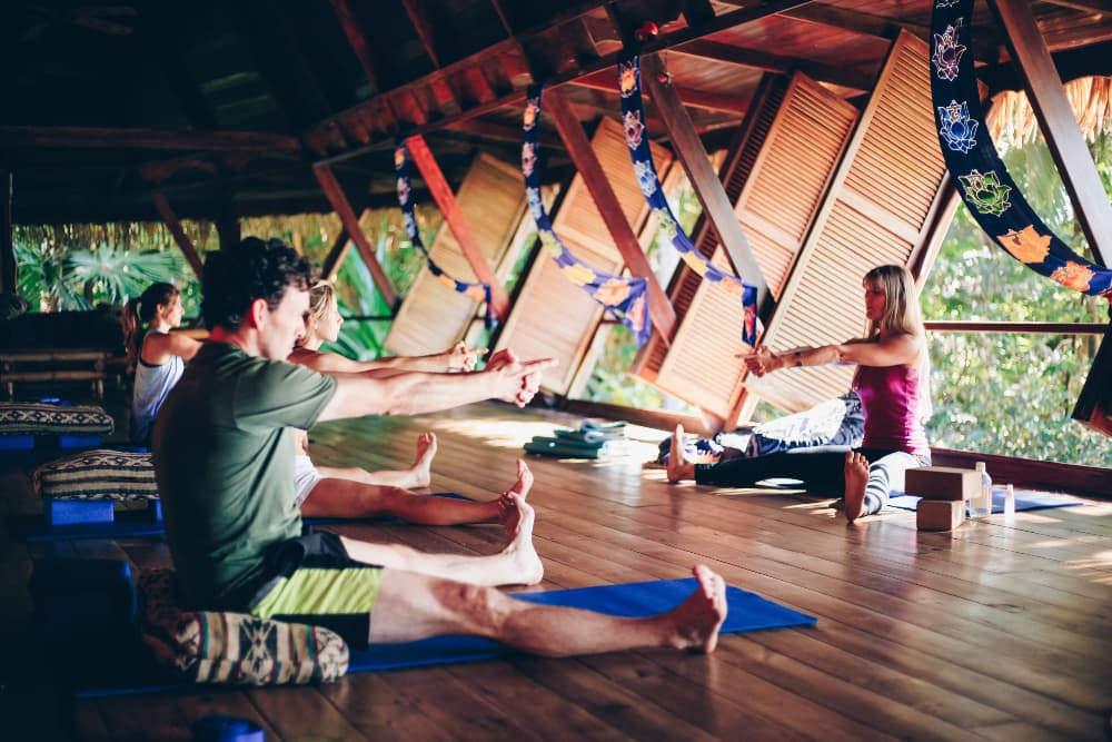 Several people doing the same yoga pose on mats with a teacher leading in front of the room