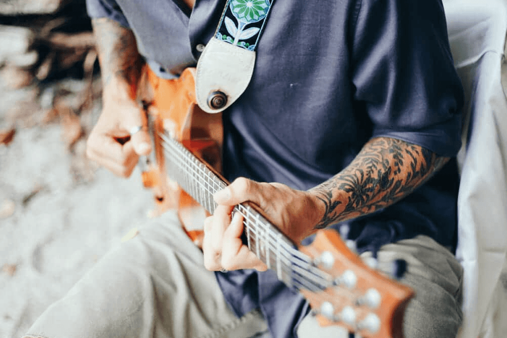 Man with tattoos, sitting playing guitar in blue shirt