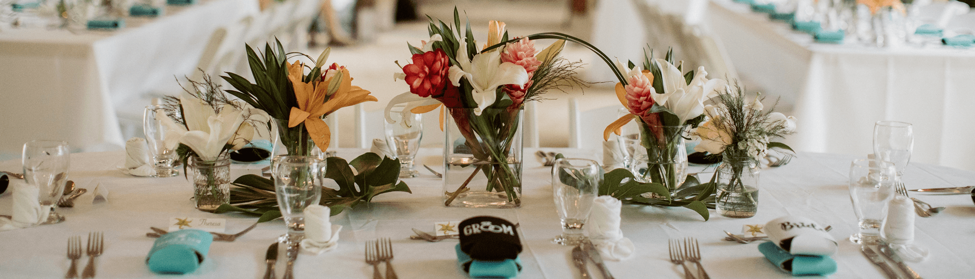 Tropical Flowers arranged on table with place settings on top of white table cloth