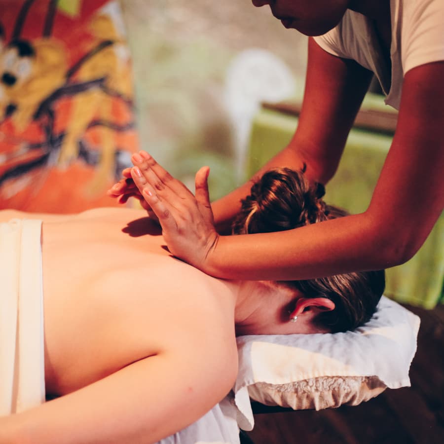 A woman with her hair in a bun and draped in a white sheet having her upper back massaged