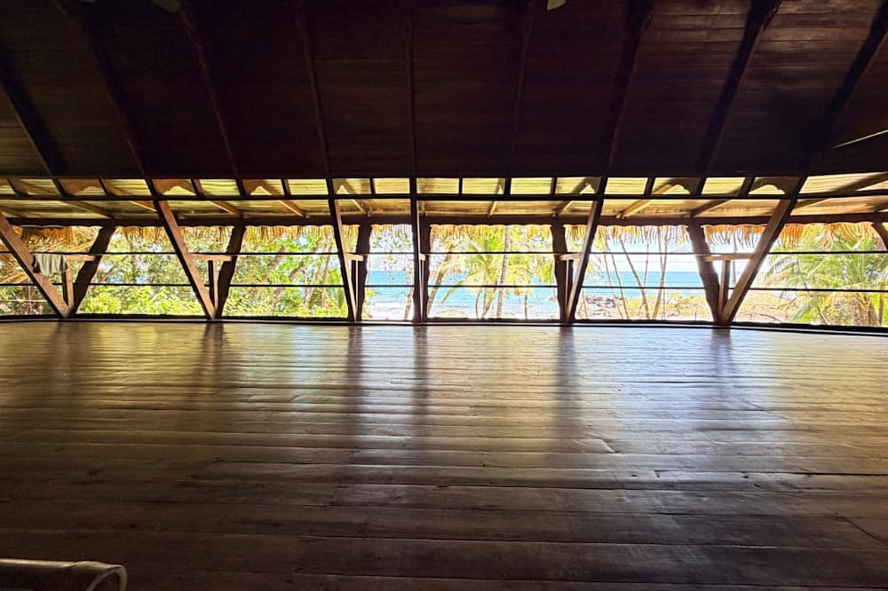 Wooden floor viewed from an open room showcasing tropical foliage and a glimpse of the sea.