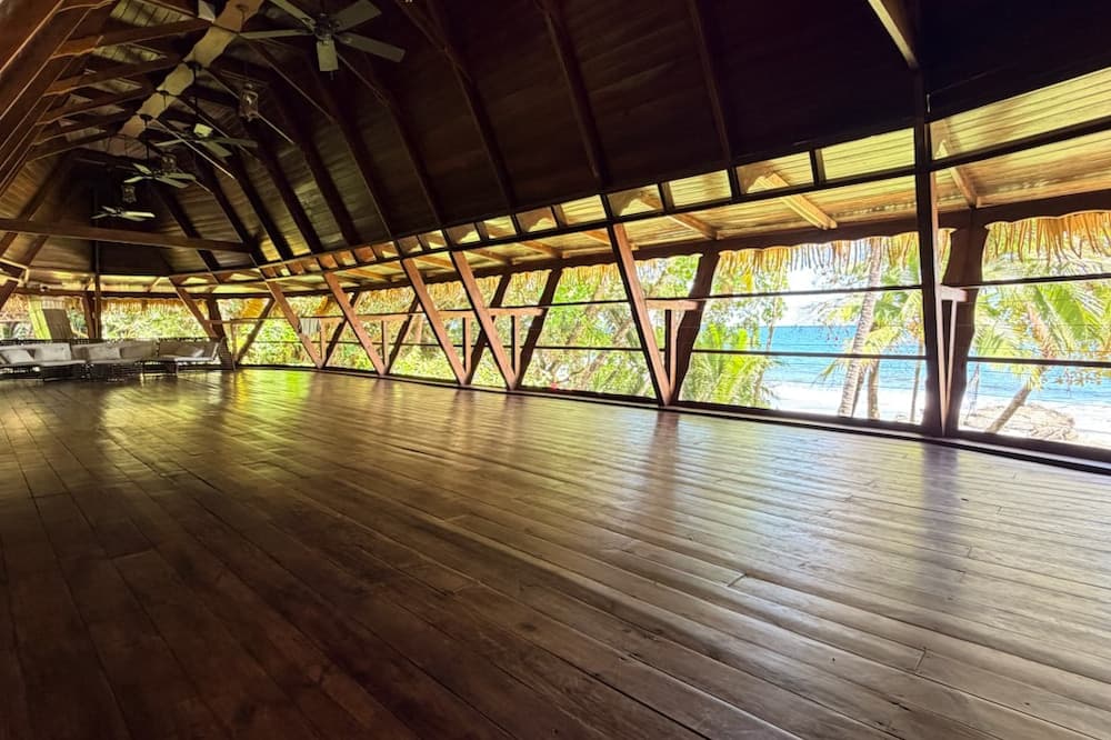 A spacious wooden interior with large windows overlooking a beach and palm trees.