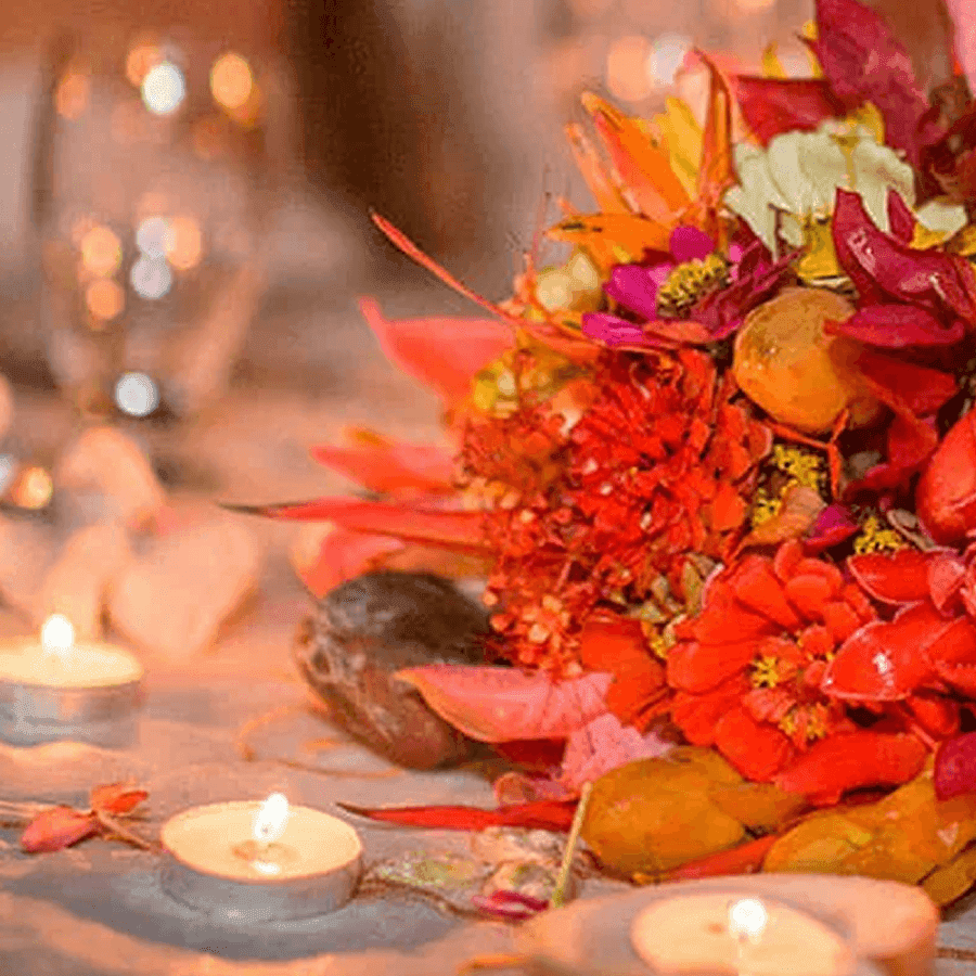 A vibrant floral arrangement with orange, red, and purple blossoms surrounded by candles.