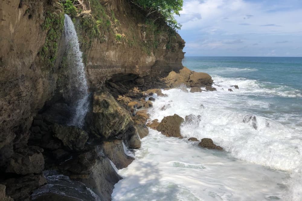 A waterfall gushing over a rocky cliff into the crashing waves below