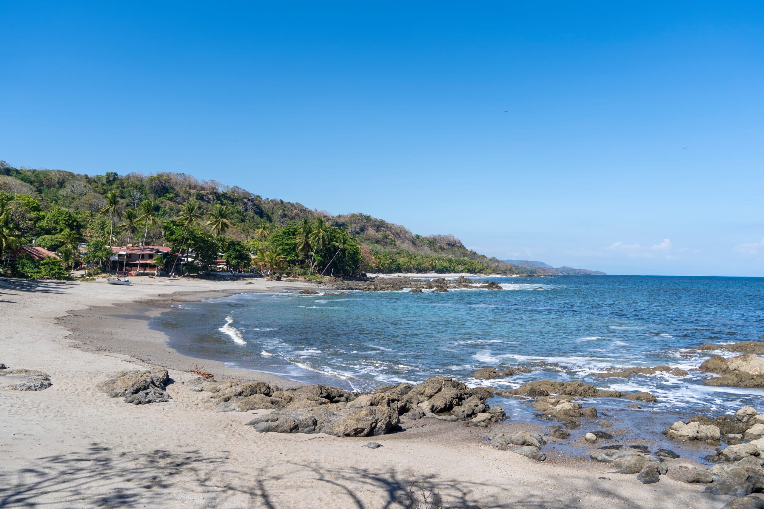 A serene beach scene with sandy shores, rocky outcrops, and calm blue waters under a clear sky.