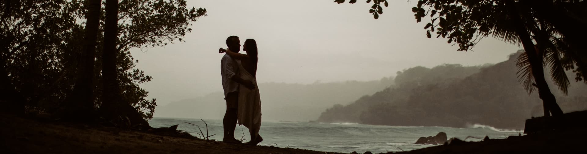 A silhouetted couple embraces on a beach with a misty ocean backdrop.