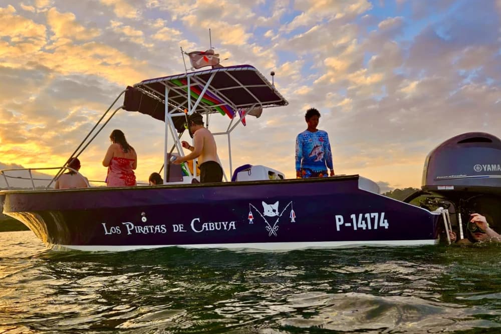 Several people in swimsuits and rash guards on a boat at sunset